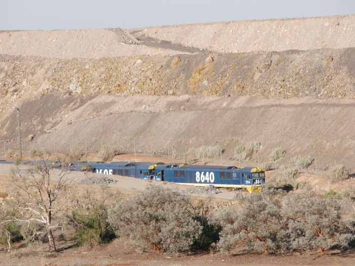 
The giant slag and overburden heap from the mines dwarfs 8640 and 8605 at
the head of a conga line of withdrawn 86 class locos stored on a siding
next to the main line.
