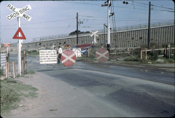 The gates at Camellia were manually worked, no matter what the weather. Here the station staff are closing the gates for an up train approaching. 