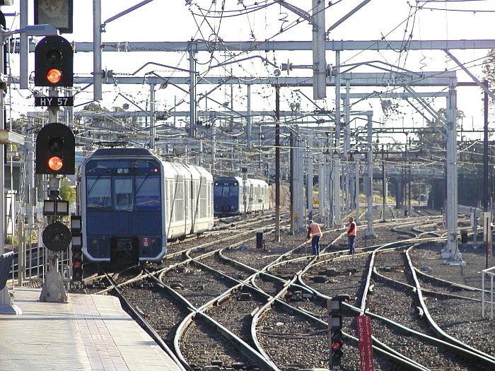 
Tangara urban set T3 has just departed and is making its way through the yard.
Meanwhile a pair of workers are checking the track.
